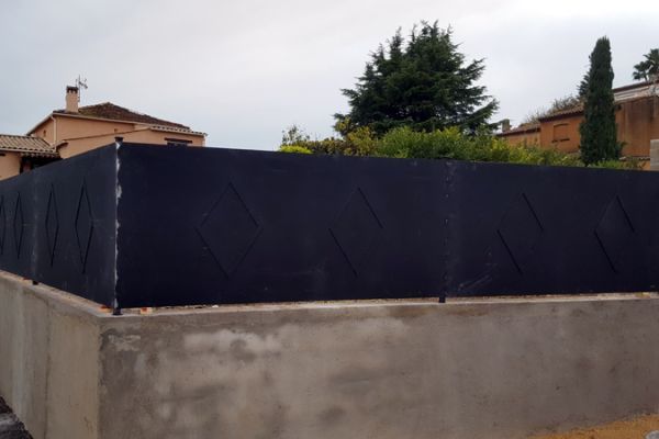 Clôture en fer forgé moderne avec motifs en losange, installée sur un muret en béton, conçue par Ferronnerie Ferafer.